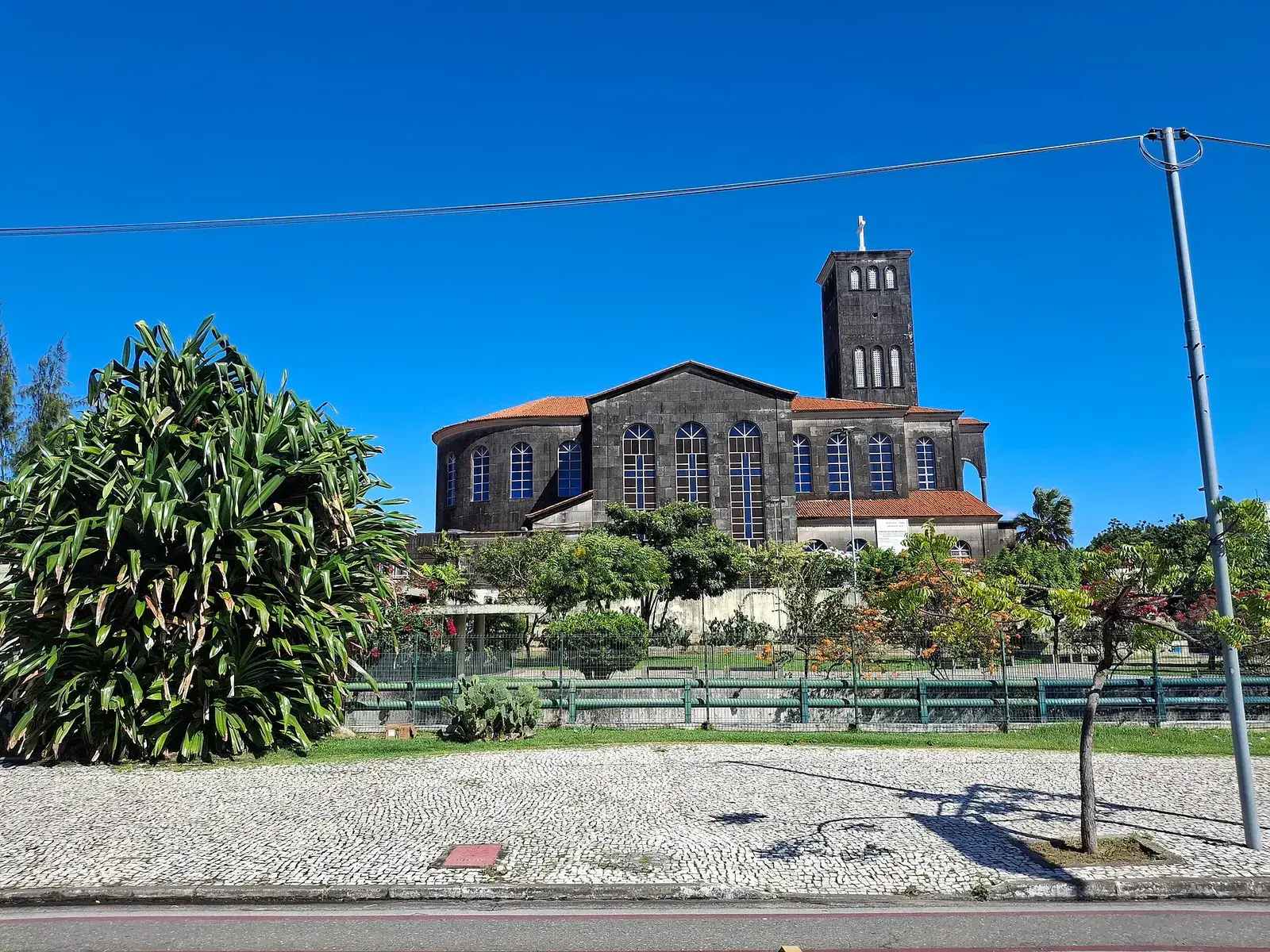 La chiesa in mattoni di São Benedito con un’alta torre quadrata dietro un giardino con palme