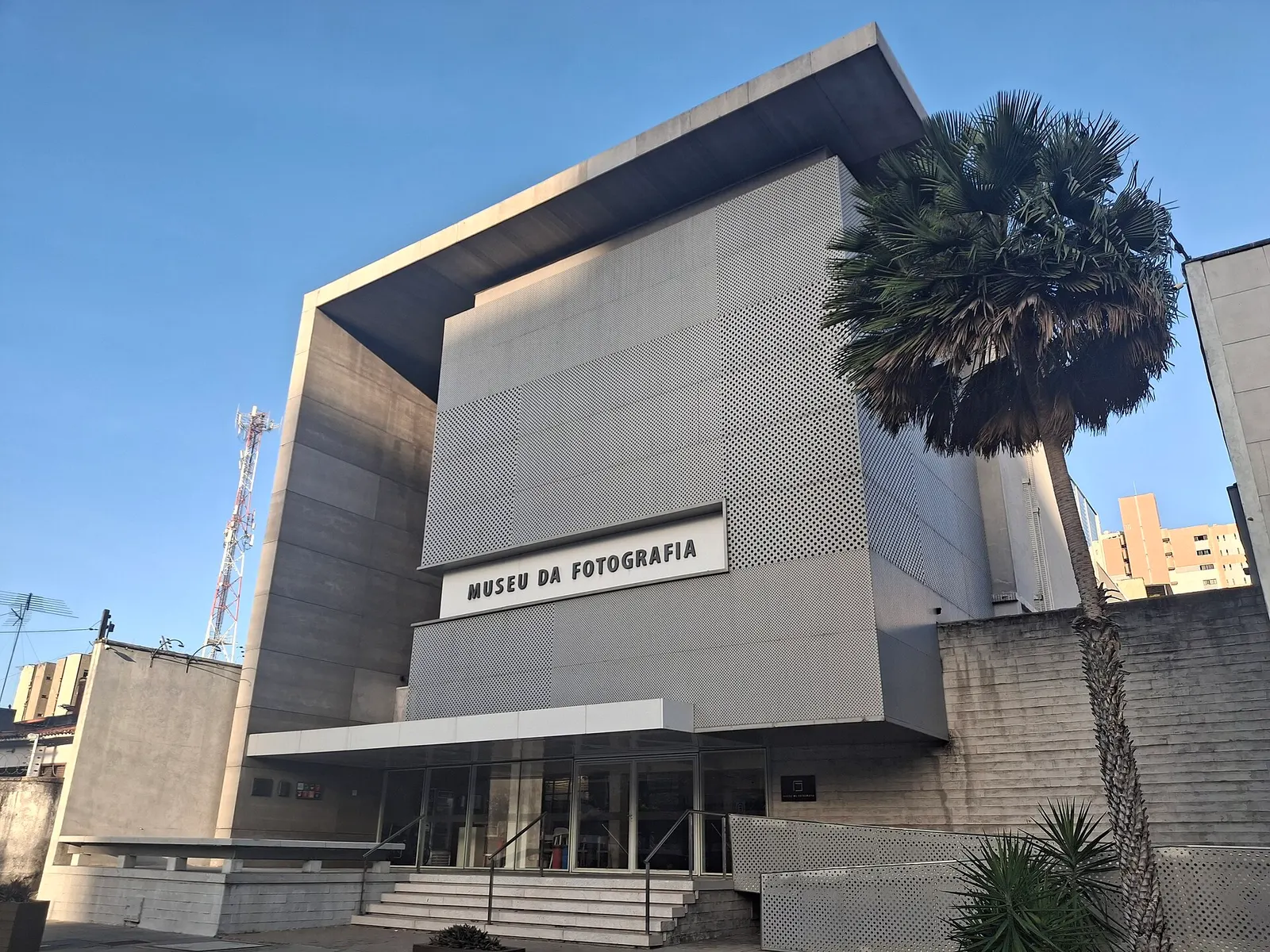 The grey facade of Museu da Fotografia Fortaleza with a palm tree in front