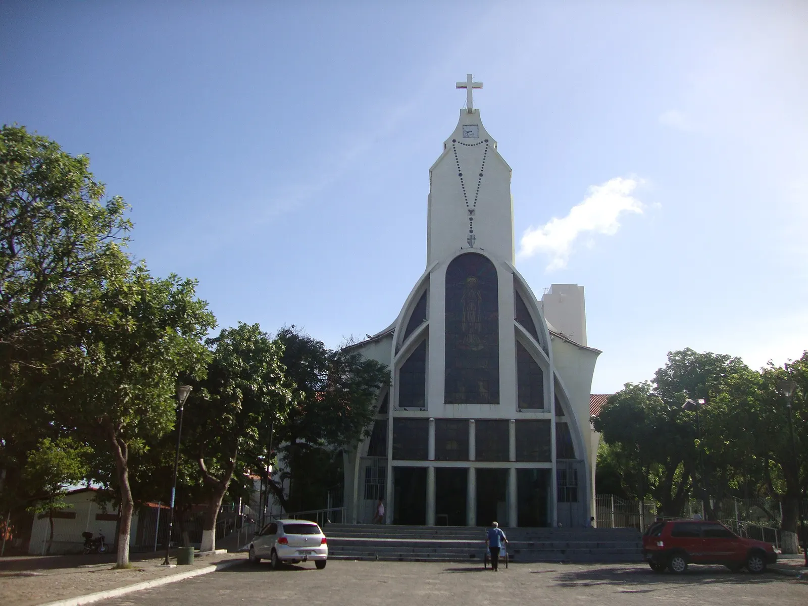 La fachada blanca y puntiaguda del santuario de Fátima con un rosario y una cruz